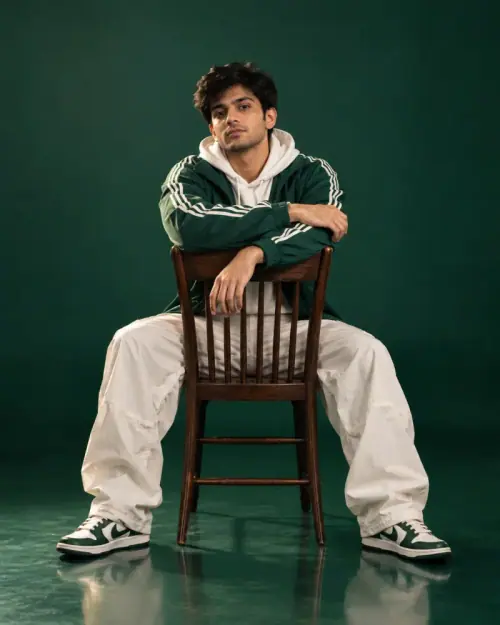 Green Track Jacket AI Prompt showing a confident man seated backward on a wooden chair in a green streetwear studio setting